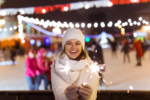 Girl holding a sparkler in her hand. Outdoor winter city background, snow, snowflakes