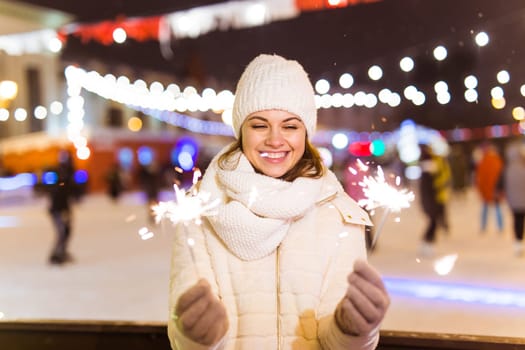 Girl holding a sparkler in her hand. Outdoor winter city background, snow, snowflakes