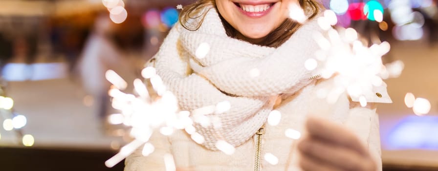 Girl holding a sparkler in her hand. Outdoor winter city background, snow, snowflakes