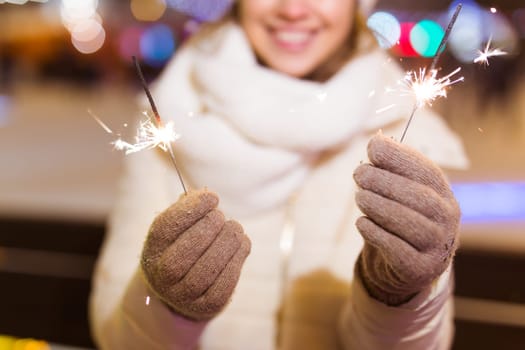 young woman wearing winter knitted clothes holding sparkler outdoors over snow background. Christmas holidays.