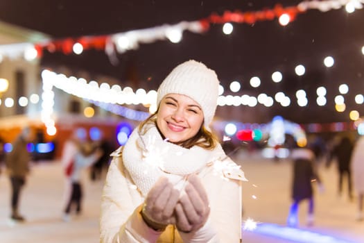 Girl holding a sparkler in her hand. Outdoor winter city background, snow, snowflakes