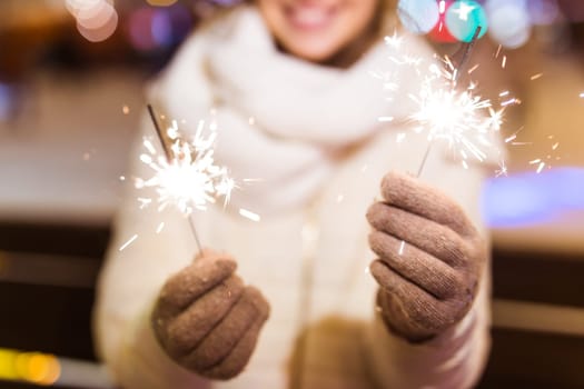 Young beautiful woman in knitted hat and scarf standing in the city with bengal light, sparkler. Concept celebration and christmas