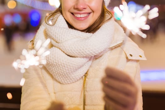 Young beautiful woman in knitted hat and scarf standing in the city with bengal light, sparkler. Concept celebration and christmas