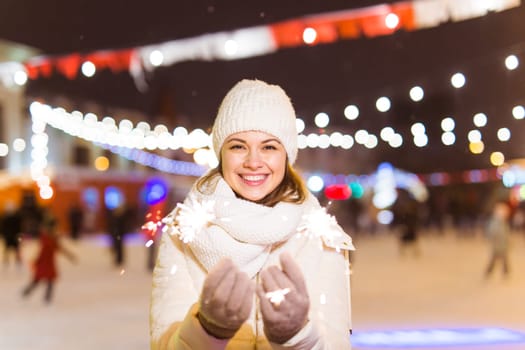 Girl holding a sparkler in her hand. Outdoor winter city background, snow, snowflakes