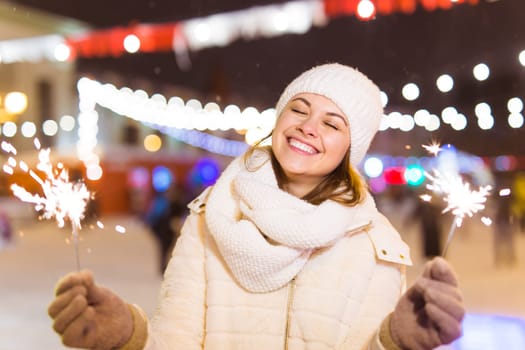 Girl holding a sparkler in her hand. Outdoor winter city background, snow, snowflakes