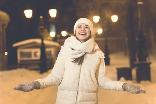 Girl having fun christmas decoration lights street. Young happy smiling woman wearing stylish knitted scarf and jacket outdoors. Model laughing. Winter wonderland city scene, New Year party.