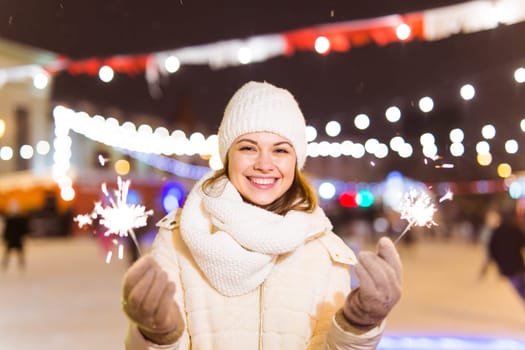 Young beautiful woman in knitted hat and scarf standing in the city with bengal light, sparkler. Concept celebration and christmas