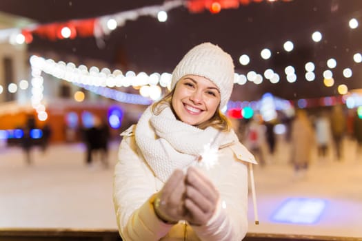 Girl holding a sparkler in her hand. Outdoor winter city background, snow, snowflakes