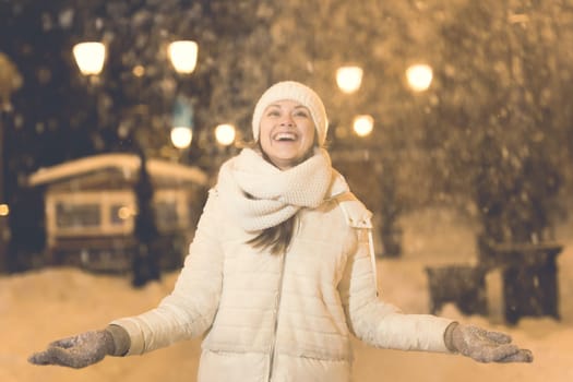 Girl having fun christmas decoration lights street. Young happy smiling woman wearing stylish knitted scarf and jacket outdoors. Model laughing. Winter wonderland city scene, New Year party.