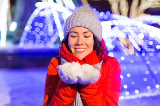 Happy funny young woman with winter clothes background evening city lights illumination. Christmas and winter holidays.