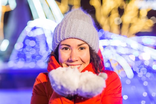 Girl having fun christmas decoration lights street. Young happy smiling woman wearing stylish knitted scarf and jacket outdoors. Model laughing. Winter wonderland city scene, New Year party.
