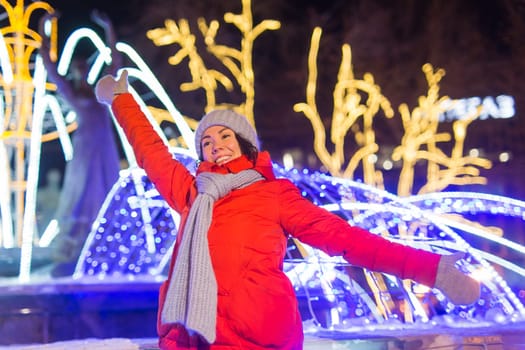 Girl having fun christmas decoration lights street. Young happy smiling woman wearing stylish knitted scarf and jacket outdoors. Model laughing. Winter wonderland city scene, New Year party.