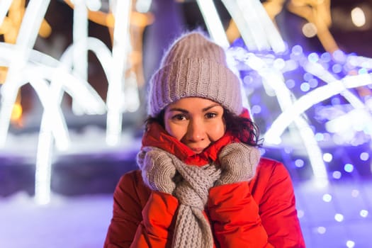 Girl having fun christmas decoration lights street. Young happy smiling woman wearing stylish knitted scarf and jacket outdoors. Model laughing. Winter wonderland city scene, New Year party.