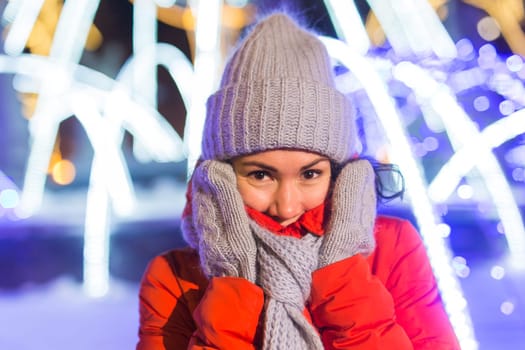 Happy funny young woman with winter clothes background evening city lights illumination. Christmas and winter holidays.