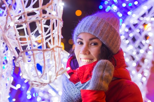 Happy funny young woman with winter clothes background evening city lights illumination. Christmas and winter holidays.