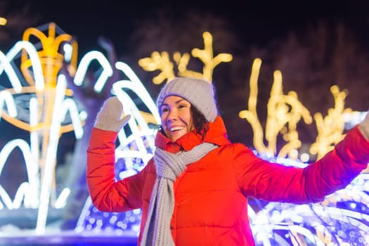 Happy funny young woman with winter clothes background evening city lights illumination. Christmas and winter holidays.