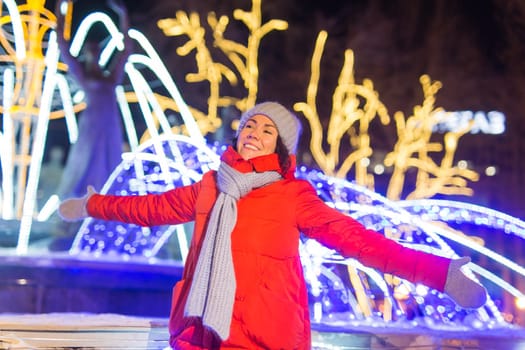 Winter holiday season. Christmas, New Year concept. Funny woman spend time having fun near illuminated and decorated showcase on city street.