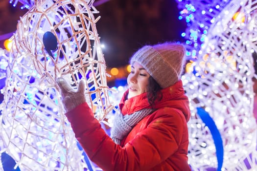 Happy funny young woman with winter clothes background evening city lights illumination. Christmas and winter holidays.