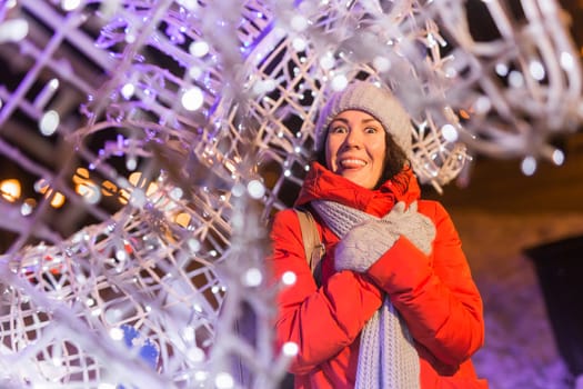 Happy funny young woman with winter clothes background evening city lights illumination. Christmas and winter holidays.