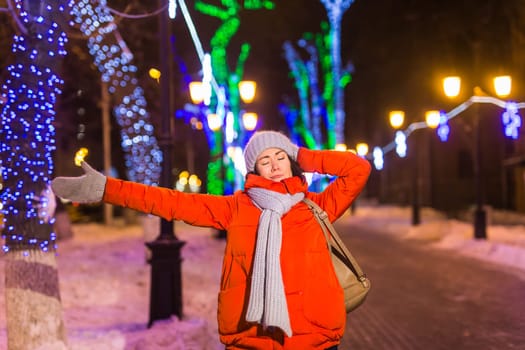 Winter holiday season. Christmas, New Year concept. Funny woman spend time having fun near illuminated and decorated showcase on city street.