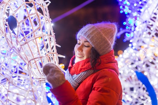 Winter holiday season. Christmas, New Year concept. Funny woman spend time having fun near illuminated and decorated showcase on city street.