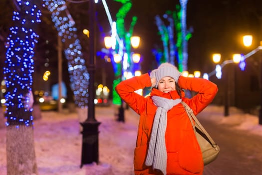 Happy funny young woman with winter clothes background evening city lights illumination. Christmas and winter holidays.