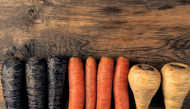 Three different root vegetables on a rustic wooden kitchen table on a dark background with space for text or image, healthy food or vegan ingredients concept, cover image, vegetarian food