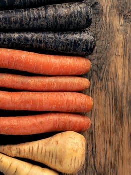Three different root vegetables on a rustic wooden kitchen table on a dark background with space for text or image, healthy food or vegan ingredients concept, cover image, vegetarian food