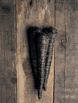 Black root vegetables on a rustic wooden kitchen table view from above with space for text or image, healthy food or vegan ingredients concept, cover image, vegetarian food