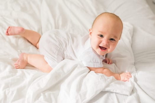 Adorable baby boy in white sunny bedroom. Newborn child relaxing in bed. Nursery for young children. Textile and bedding for kids. Family morning at home