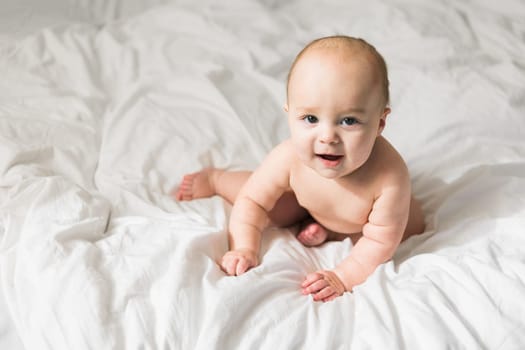 Adorable baby boy in white sunny bedroom. Newborn child relaxing in bed. Nursery for young children. Textile and bedding for kids. Family morning at home