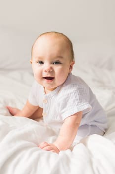Adorable baby boy in white sunny bedroom. Newborn child relaxing in bed. Nursery for young children. Textile and bedding for kids. Family morning at home
