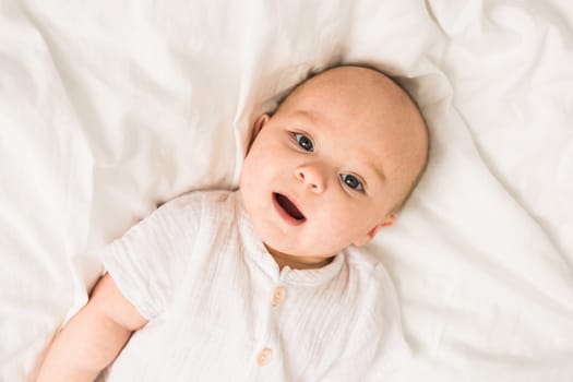 Adorable baby boy in white sunny bedroom. Newborn child relaxing in bed. Nursery for young children. Textile and bedding for kids. Family morning at home