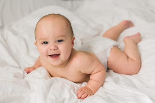 Adorable baby boy in white sunny bedroom. Newborn child relaxing in bed. Nursery for young children. Textile and bedding for kids. Family morning at home