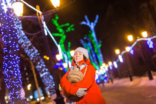 Happy funny young woman with winter clothes background evening city lights illumination. Christmas and winter holidays.