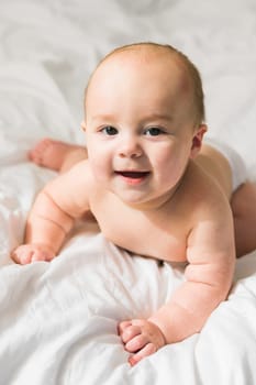 Adorable baby boy in white sunny bedroom. Newborn child relaxing in bed. Nursery for young children. Textile and bedding for kids. Family morning at home