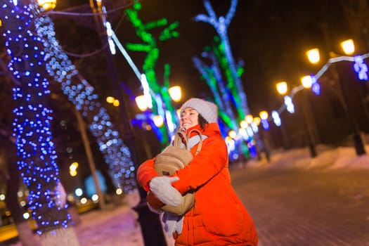 Girl having fun christmas decoration lights street. Young happy smiling woman wearing stylish knitted scarf and jacket outdoors. Model laughing. Winter wonderland city scene, New Year party.