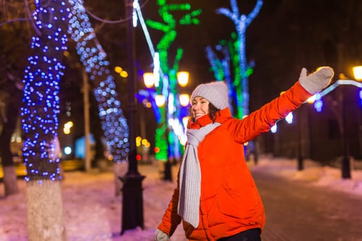 Happy funny young woman with winter clothes background evening city lights illumination. Christmas and winter holidays.