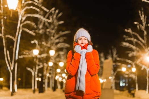 Happy funny young woman with winter clothes background evening city lights illumination. Christmas and winter holidays.