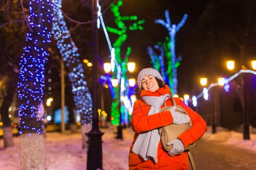 Winter holiday season. Christmas, New Year concept. Funny woman spend time having fun near illuminated and decorated showcase on city street.