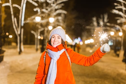 Girl holding a sparkler in her hand. Outdoor winter city background, snow, snowflakes