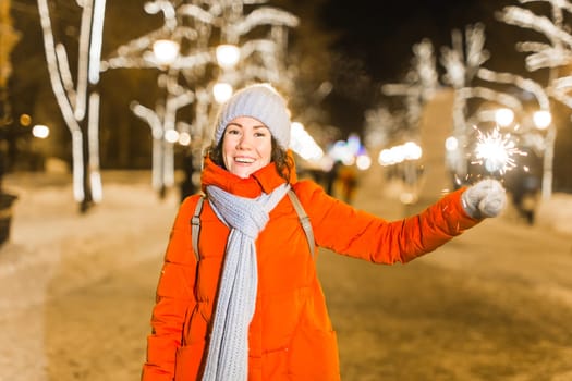 Young beautiful woman in knitted hat and scarf standing in the city with bengal light, sparkler. Concept celebration and christmas