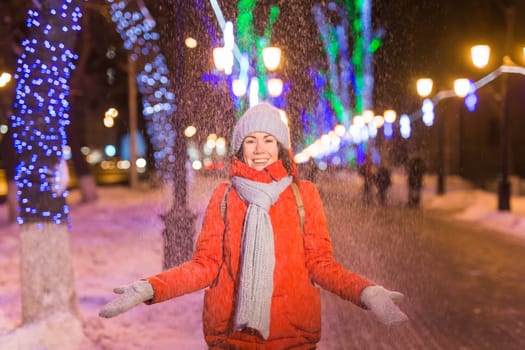 Girl having fun christmas decoration lights street. Young happy smiling woman wearing stylish knitted scarf and jacket outdoors. Model laughing. Winter wonderland city scene, New Year party.