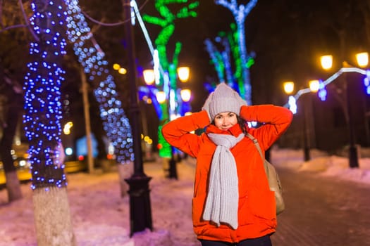 Happy funny young woman with winter clothes background evening city lights illumination. Christmas and winter holidays.
