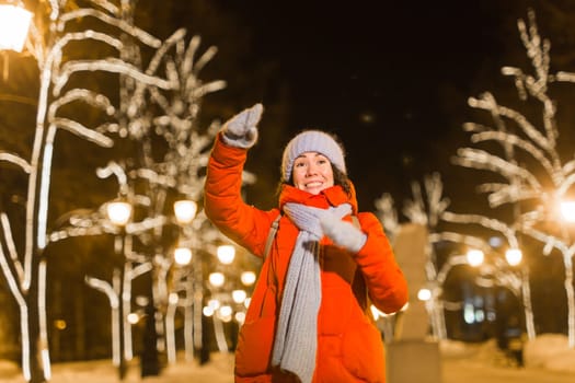 Happy funny young woman with winter clothes background evening city lights illumination. Christmas and winter holidays.