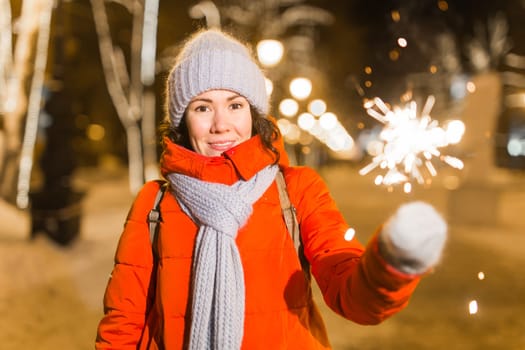 Girl holding a sparkler in her hand. Outdoor winter city background, snow, snowflakes