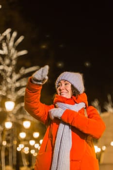Girl having fun christmas decoration lights street. Young happy smiling woman wearing stylish knitted scarf and jacket outdoors. Model laughing. Winter wonderland city scene, New Year party.