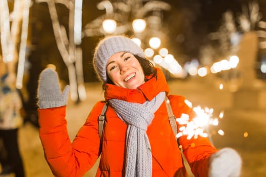 Girl holding a sparkler in her hand. Outdoor winter city background, snow, snowflakes