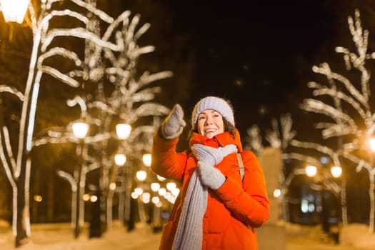Winter holiday season. Christmas, New Year concept. Funny woman spend time having fun near illuminated and decorated showcase on city street.