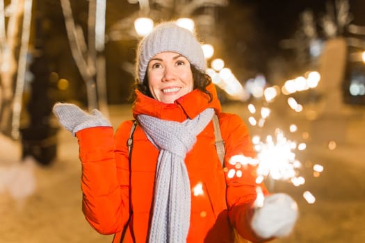 Girl holding a sparkler in her hand. Outdoor winter city background, snow, snowflakes